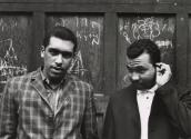 Gang Series (two men in front of wood wall of graffitti) 
