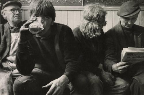 Young man sipping beer on bench next to other patrons, Glasgow, Scotland