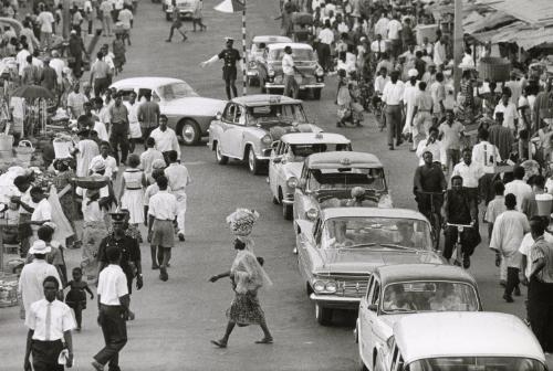 Street scene with cars in traffic and woman balancing a basket on her head, Ghana