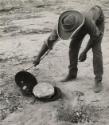 Aboriginal man baking damper (bush bread) in a campoven (cast-iron pot with lid) outdoors by an open fire, Australia