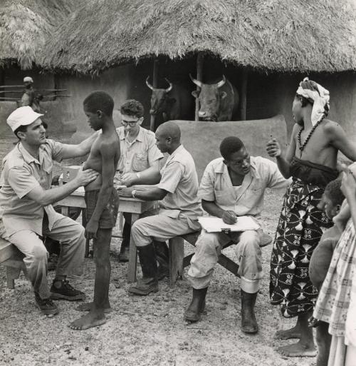UNICEF doctors examine patients in front of a barn housing oxen, Nigeria, Africa