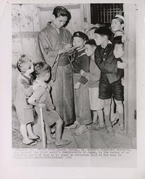 Their Hero: Yoshio Shirai, 28, world's flyweight champion, who brought the first wold's championship to Japan, is the center of an admiring group of boys as he signs an autograph book at his home in Tokyo.