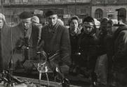 Jerusalem Alley, A Symbolic Warsaw Street: when Soviet and Polish troops met in Warsaw on January 17, 1945, it was in Jerusalem Alley that they met. At that time, Warsaw was 95% destroyed and this street, like the rest, was like a cemetery in the city of the dead. But today, 15 years later, the scene has changed considerably. There are still a few ruins to be seen, true, but for the most part, the street has been entirely rebuilt. Most of the older buildings are in the grimly-blunt Soviet-style of architecture; but in more recent structures, even this changed. And since the October 1956 revolution, a new wind of dignity and freedom has blown down the street. It is no longer an eastern city, nor is it entirely a western one. But one thing is certain, it is Polish. Pictured: a shoe store window draws a big crowd in goods hungry Warsaw.